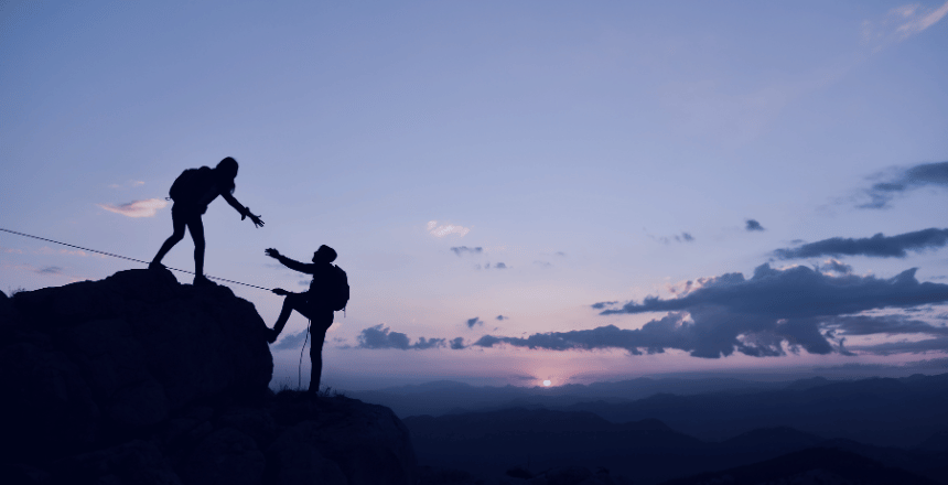 mountain climbers helping each other at dusk