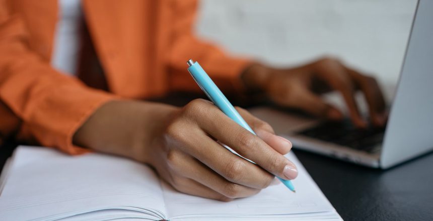 Close-up shot of student hand holding pen and writing in notebook, working at home. E-learning